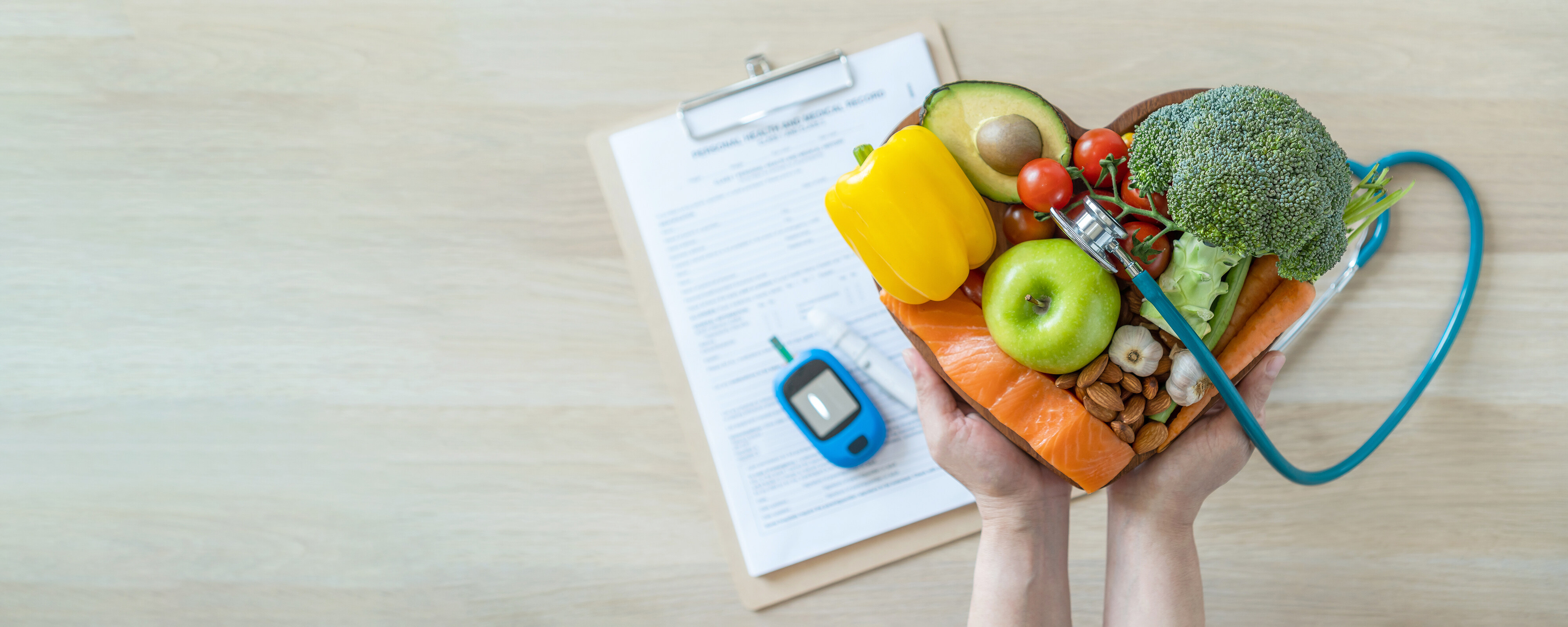 A heart-shaped bowl of colourful vegetables and food with a stethoscope and medical documents in the background